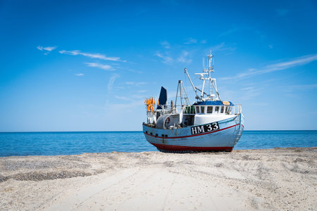 Light blue fishing boat on the beach, blue sky, horizontal