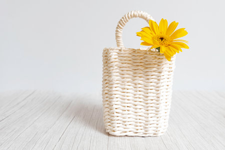 A white small basket with a yellow flower peeking out on a white wooden floor, white background, horizontalの写真素材