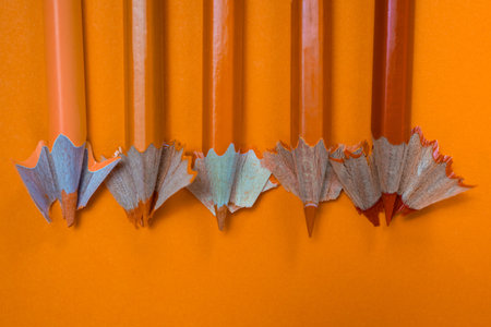 Five different orange colored pencils with sharpening chips next to each other on an orange...