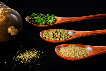 Three brown wooden spoons with different varieties of pepper on them, black background, horizontalの写真素材