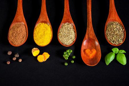 Five wooden spoons with spices on them, the fourth of which is slightly out and decorated with red spice powder in the shape of a heart, black background, horizontalの写真素材
