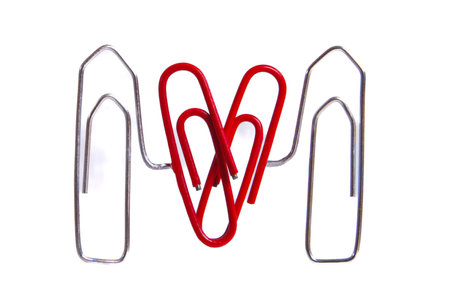 4 paper clips, two made of metal, hold two red ones, which are heart-shaped, between them, white background, horizontalの写真素材