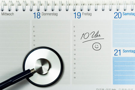 Partial view of a desk calendar with an appointment written on it and the end of a stethoscope visible, horizontalの写真素材