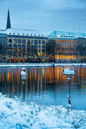 Vertical view of the Lombard Bridge sign covered in snow, in the background Christmas lights and illuminated house facades in Hamburg in winter, reflected in the water, verticalの写真素材