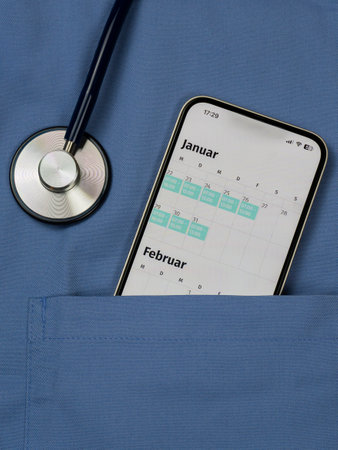 A smartphone showing the roster sticks out of a blue coat pocket, part of a stethoscope in the picture, verticallyの写真素材