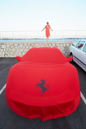 Ferrari red cloth cover at the harbor with woman in Cannes, France. Ferrari emblem is the rampant horse.のeditorial素材