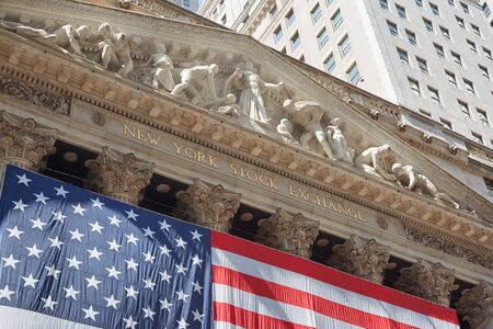New York Stock Exchange building sign with big US flag, financial district in New York in a sunny...