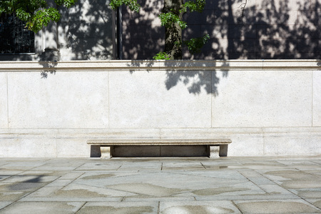 Empty stone bench with light stone background and tree leaves shadows in a sunny dayの写真素材