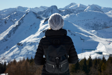 Woman with wool hat and backpack looking at mountains with snow in a sunny winter dayの写真素材
