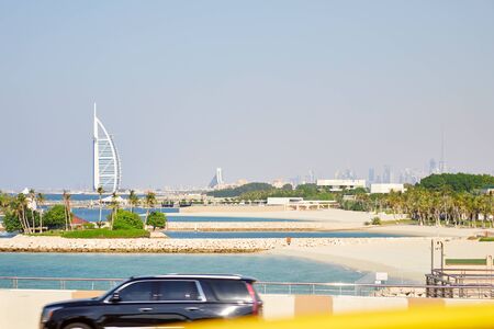 DUBAI, UNITED ARAB EMIRATES - NOVEMBER 23, 2019: Burj Al Arab luxury hotel with palm trees and Dubai city skyline in a sunny dayのeditorial素材