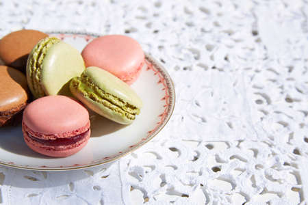 Macarons biscuits with ceramic saucer and white embroidered tablecloth in sunlightの写真素材