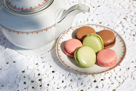 Macarons biscuits with ceramic saucer and teapot, white embroidered tableclothの写真素材
