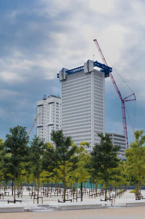 Under Construction skyscraper in Rotterdam with blue high scaffolding close to a green modern design...