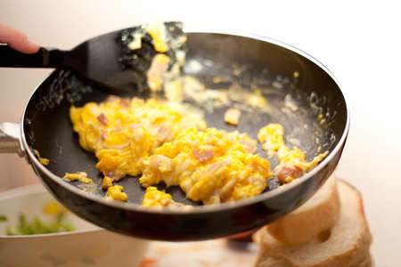 Scrambled eggs and bacon in metal black cooking pan Italian Food Made in Italy with bread and salad on tableの写真素材