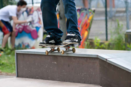 Skater Grinding 50 50 on wall in Skate park with graffiti painter behindの写真素材
