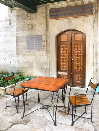Metal and wooden table with two Arabic style chairs in front of the mosque wooden doorのeditorial素材