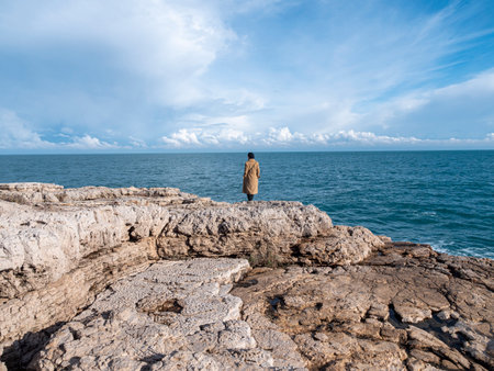 Woman isolated on the rocks looking at the sea in winter seasonの写真素材