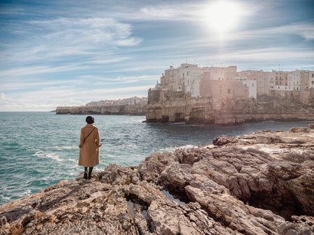 Woman isolated on the rocks looking Polignano a mare in winter seasonの写真素材