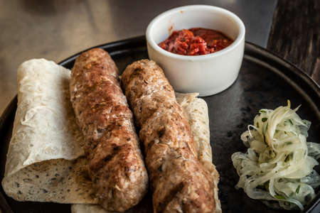 Two lula kebabs on pita bread with onions and red tomato sauce