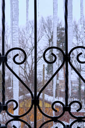 Large icicles behind a cast-iron grate against a blurred background of a suburban landscape. Selective focusの写真素材