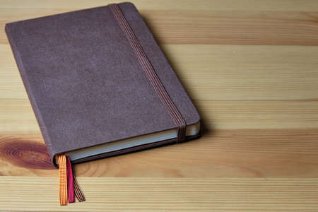 Brown notebook with an elastic band and multi-colored bookmarks on a wooden table. Copyspaceの写真素材