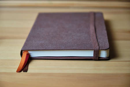 Brown notebook with an elastic band and multi-colored bookmarks on a wooden table. Selective focus. Space for lettering and designの写真素材