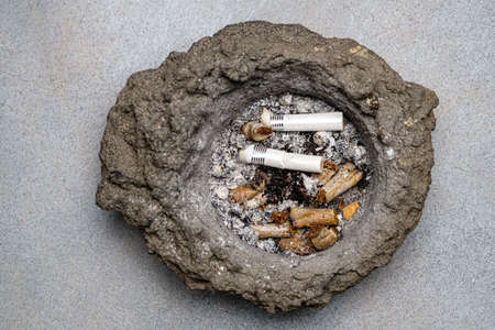 Various cigarette butts in an old, dirty ashtray of volcanic lava. Close-up. Selective focus.の写真素材