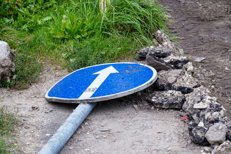 A post with a road sign - straight ahead. Fallen post with a pointer on the ground. Close-up.の写真素材