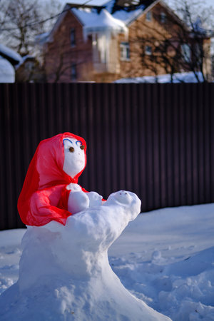 Snowman in a red shawl in the shape of a figure with a baby. Suburban winter landscape. selective focus.の写真素材