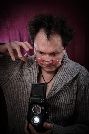 Man with retro camera in hand. Tousled crazy photographer in pink glassesの写真素材