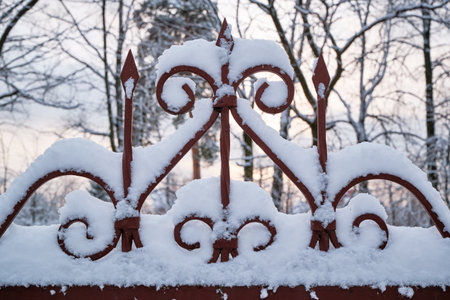 Close-up of a metal fence covered with snow against a sunset landscapeの写真素材
