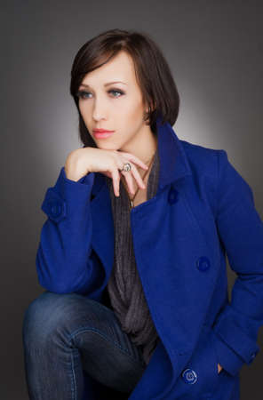 Vertical color image   Beautiful young woman deep in thoughts, wearing navy blue coat  studio portrait on grey background の写真素材