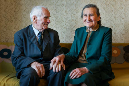 Cute 80 plus year old married couple posing for a portrait in their house. Love forever concept. 