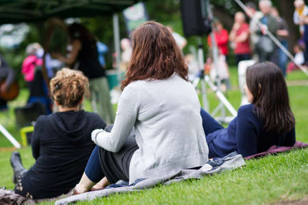 Friends sitting on the grass, enjoying an outdoors music, culture, community event, festival の写真素材