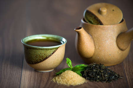 Ceramic teapot, cup of black tea with mint leaves and brown sugar on wooden tableの写真素材