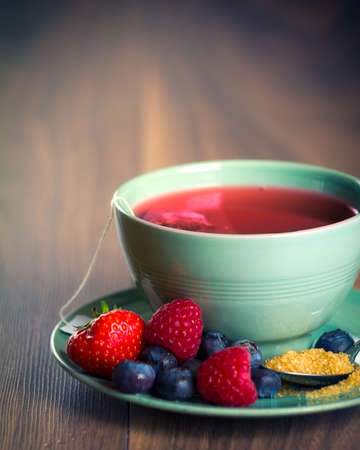 Cup of fruit tea with strawberries, raspberries and blueberries on wooden table, with copy spaceの写真素材