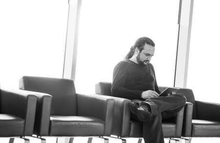 Handsome young man with dreadlocks using his digital tablet pc at an airport lounge, modern waiting room, with backlight の写真素材