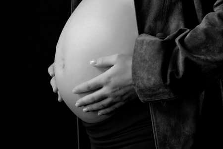 Image of pregnant woman touching her belly with hands on black backgroundの写真素材