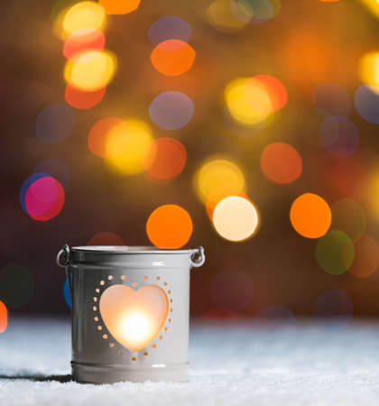 Burning candle, in snow, with defocussed fairy lights, boke in the background, Festive Christmas background with copyspaceの写真素材