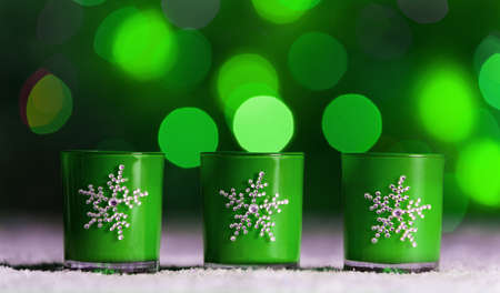 Set of 3 candles standing in snow with defocussed fairy lights, green bokeh in the background, Festive Christmas background with copyspaceの写真素材