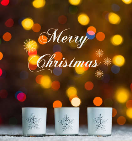 Set of 3 candles standing in snow with defocussed fairy lights, orange or golden bokeh in the background, Festive Christmas background with copyspaceの写真素材