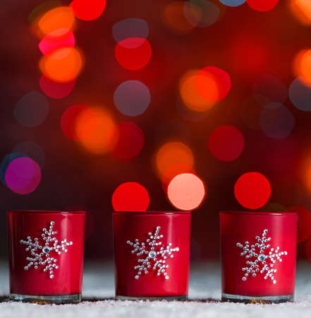 Set of 3 candles standing in snow with defocussed fairy lights, red bokeh in the background, Festive Christmas background with copyspaceの写真素材