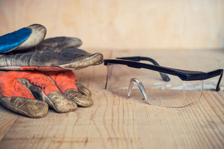 Old used safety glasses and gloves on wooden background