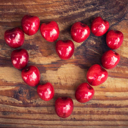 Ripe organic homegrown cherries on wooden background in heart shapeの写真素材