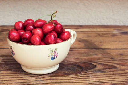 Ripe organic homegrown cherries in a vintage ceramic bowl, on wooden backgroundの写真素材