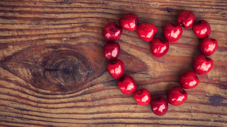 Ripe organic homegrown cherries on wooden background in heart shapeの写真素材
