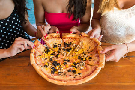 Anonymous female friends sharing a pizzaの写真素材