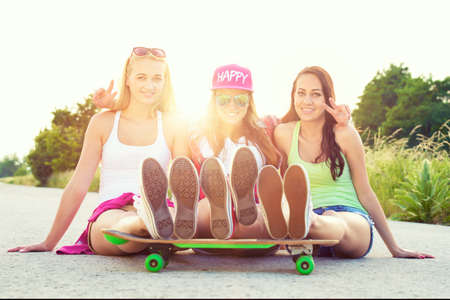 Attractive smiling hipster teenage friends with skateboard, colorised image with sunflareの写真素材