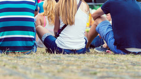 Friends sitting on the grass, enjoying an outdoors music, culture, community event, festivalの写真素材