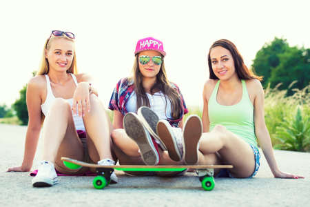 Attractive smiling hipster teenage friends with skateboard, colorised image with sunflareの写真素材